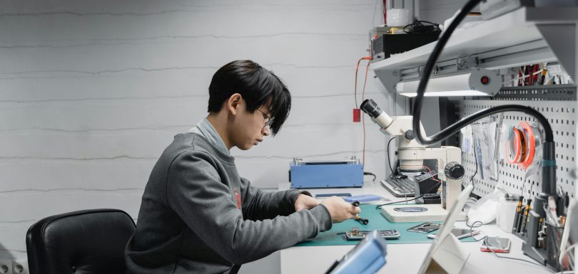 man in grew jumper looking at parts on a desk