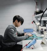 man in grew jumper looking at parts on a desk