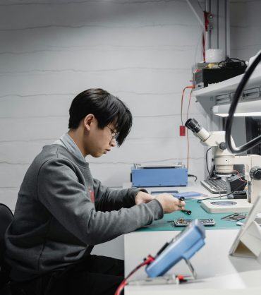 man in grew jumper looking at parts on a desk
