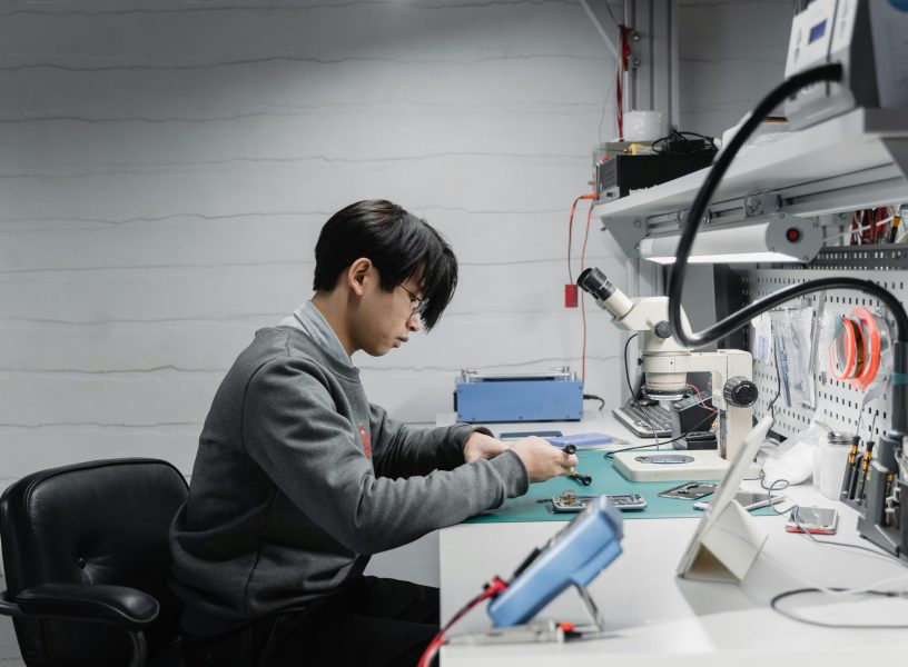man in grew jumper looking at parts on a desk